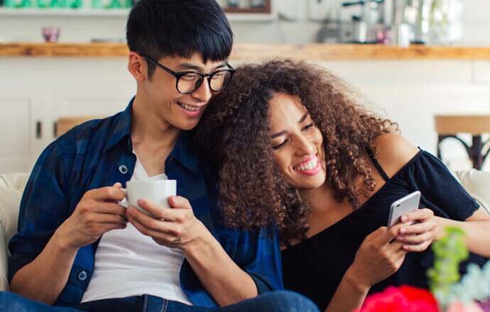 homem e mulher no sofá a olhar para o telemóvel protegido pelo Norton 360 for Mobile.